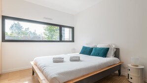 Un dormitorio moderno con cabecera de cama de madera, ropa de cama blanca, almohadas color turquesa y una mesita de noche con lámpara.