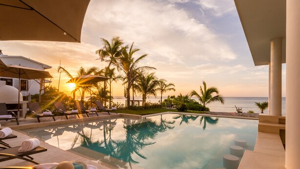 A poolside area with lounge chairs, a sunken seating area, and a view of the ocean at sunset.