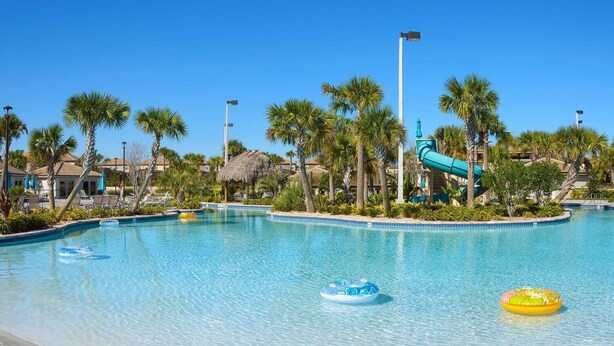 Une piscine d’un bleu éclatant, bordée de palmiers et dotée d’un toboggan aquatique.