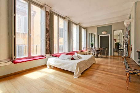 A spacious room with a large bed, wooden flooring, and a dining area with chairs and a table.