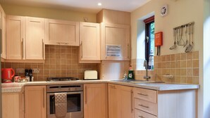 Una cocina con armarios de madera, una estufa a gas, un tostador y una ventana con utensilios colgando.