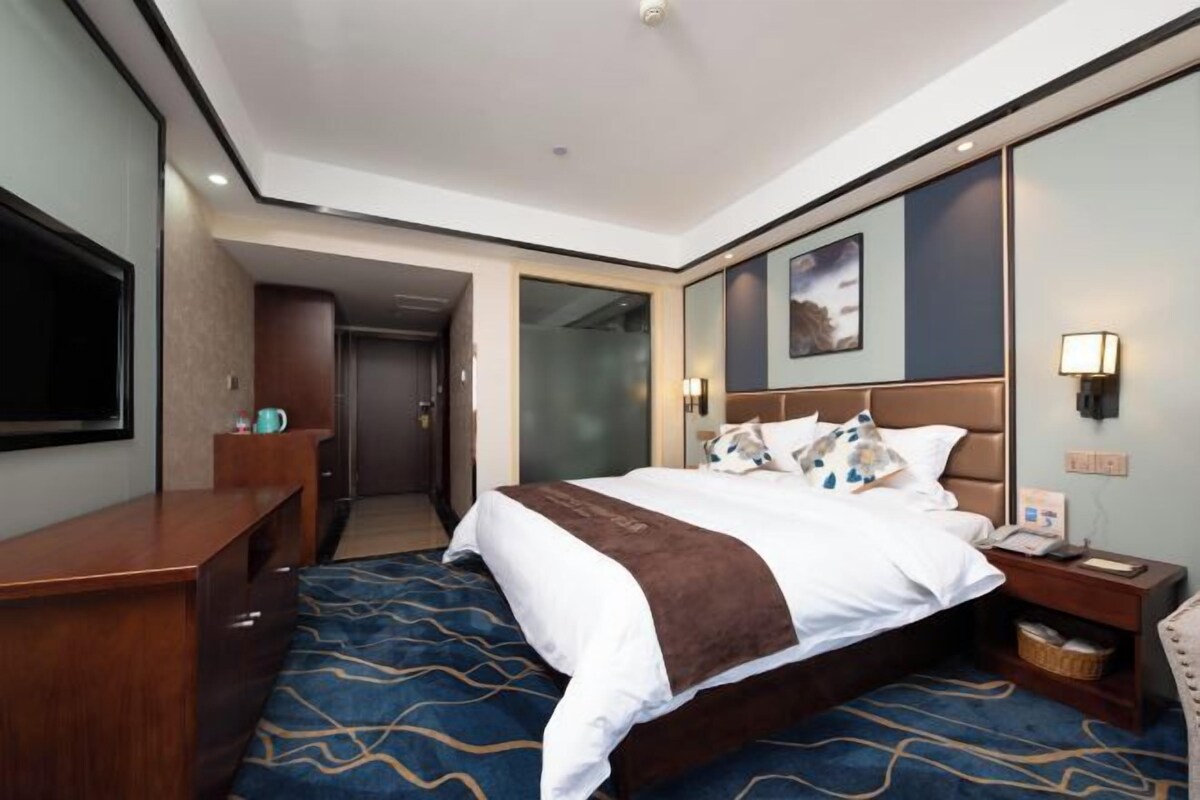 A hotel room with a bed, bedside table, lamp, and a television.