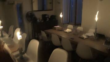 A dining area with a long table, white chairs, and candles. There is a mirror on the wall and a window with a view of the outside.