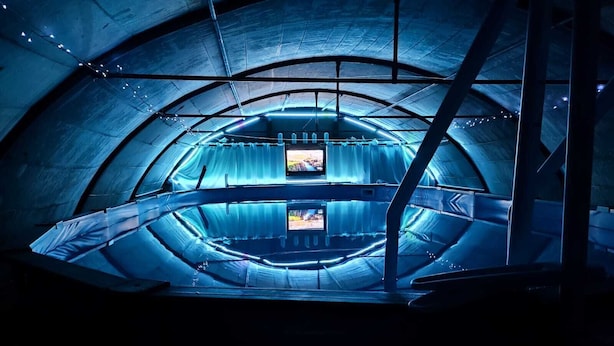 Una sala amplia y circular con una zona de estar central y una pantalla de televisión.