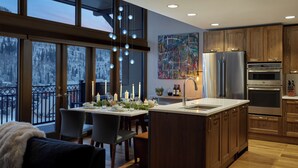 A modern kitchen with a large island, wooden cabinets, and a view of a snowy landscape through large windows. - Landmark 704 - 3 Bedroom Diamond (Vail)