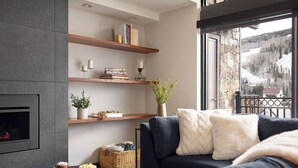 A modern living room with a fireplace, wooden shelves, a cozy sofa, and a view of a snowy landscape. - Landmark 704 - 3 Bedroom Diamond (Vail)