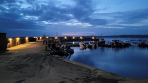 Un port de plaisance au crépuscule, avec des bateaux amarrés, une promenade en béton et une étendue d’eau calme.