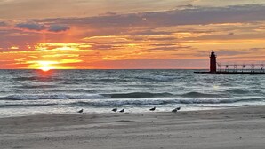 Une plage avec des vagues, un phare et un coucher de soleil.