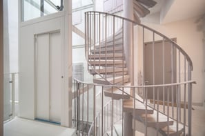 A spiral staircase with metal railings, a door at the bottom, and a view of the upper floor through glass doors.