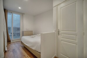 Ein Schlafzimmer mit Bett, Nachttisch, Fenster mit Ausblick und Tür.