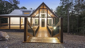 A modern house with a wooden deck leading to a front door, surrounded by trees.