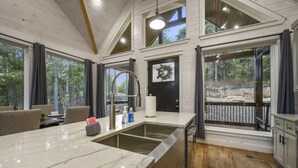A modern kitchen with a large island, a built-in oven, and a view of the forest.
