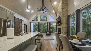 A modern kitchen with a large island, stone walls, and large windows offering a view of the outdoors.
