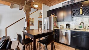 A modern kitchen with dark cabinets, stainless steel appliances, and a wooden dining table with chairs. - Alpine Manor Retreat Mountain Relaxation (Olympic Valley)