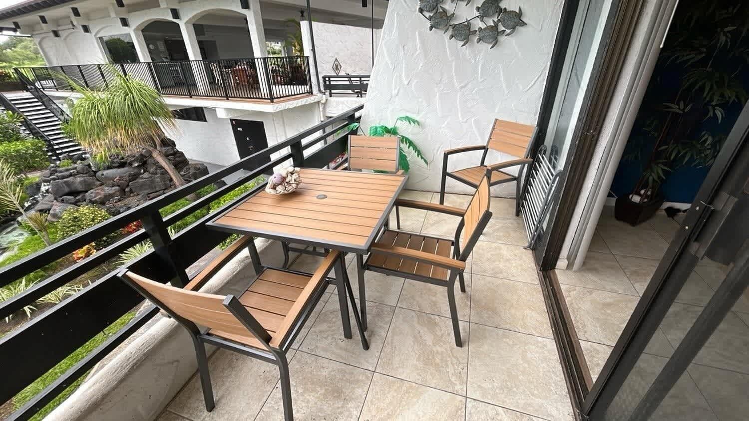 Un balcón con mesa y sillas de madera, rodeado por un muro blanco con detalles decorativos.