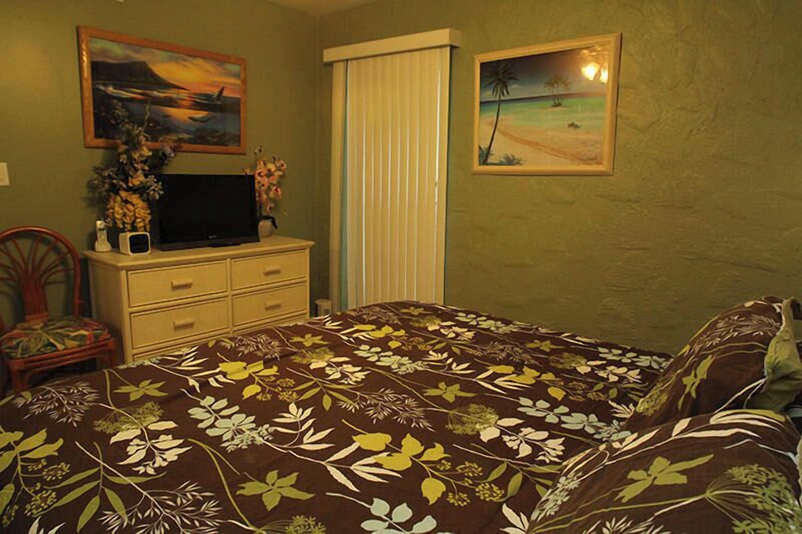Ein Schlafzimmer mit Bett, Kommode, Fernseher und zwei gerahmten Bildern an der Wand.