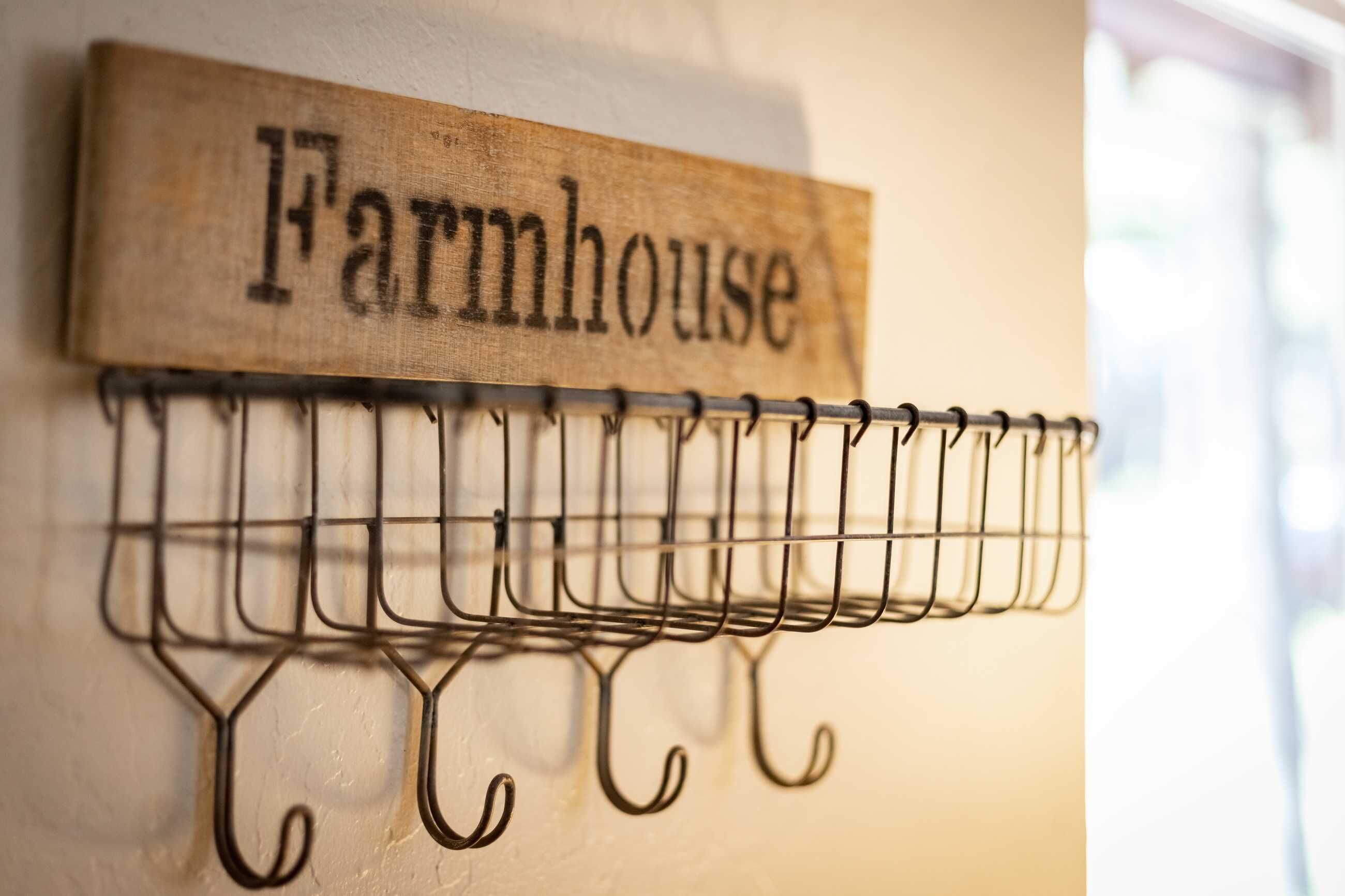 A metal rack with hooks and a wooden sign that reads "Farmhouse" mounted on a wall.