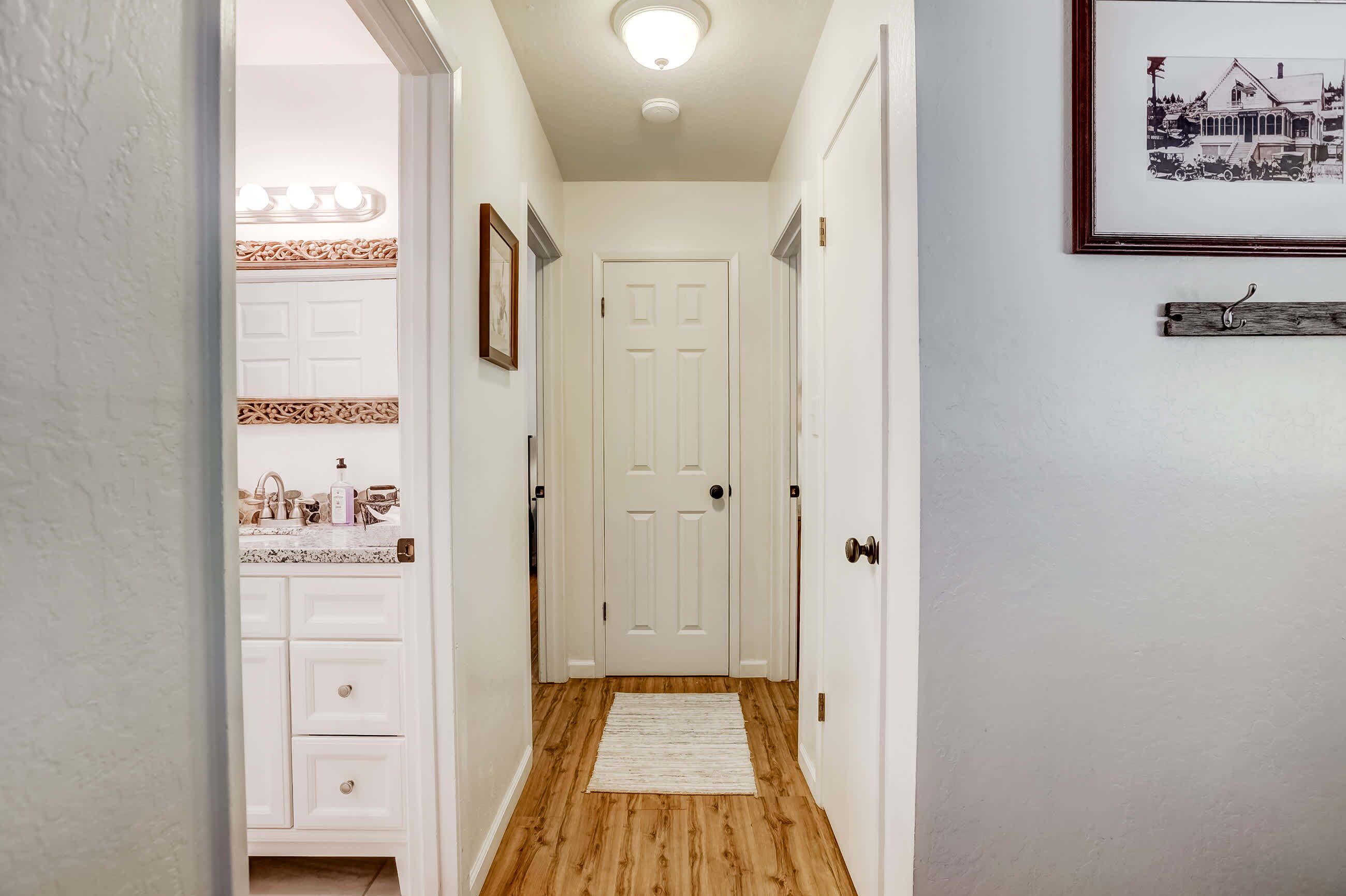 A hallway with a wooden floor, white walls, and a white door at the end.