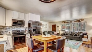 A modern kitchen with white cabinets, stainless steel appliances, and a wooden dining table with four chairs. - Coziness Cabin - Cute Little Cabin in the Tahoe Woods! (South Lake Tahoe)