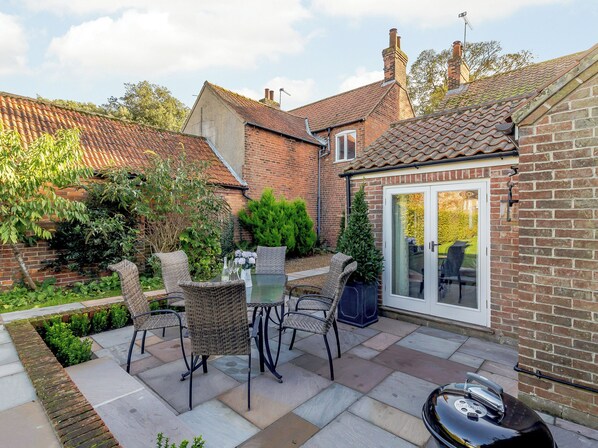 A patio with outdoor furniture, a barbecue grill, and a brick house with a tiled roof.