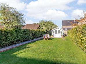 A well-maintained garden with a small white gazebo, a grassy lawn, and a hedge-lined pathway.