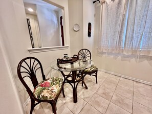 Enjoy meals in this dining area with a round table and four chairs, surrounded by a white tiled floor and sheer curtains.