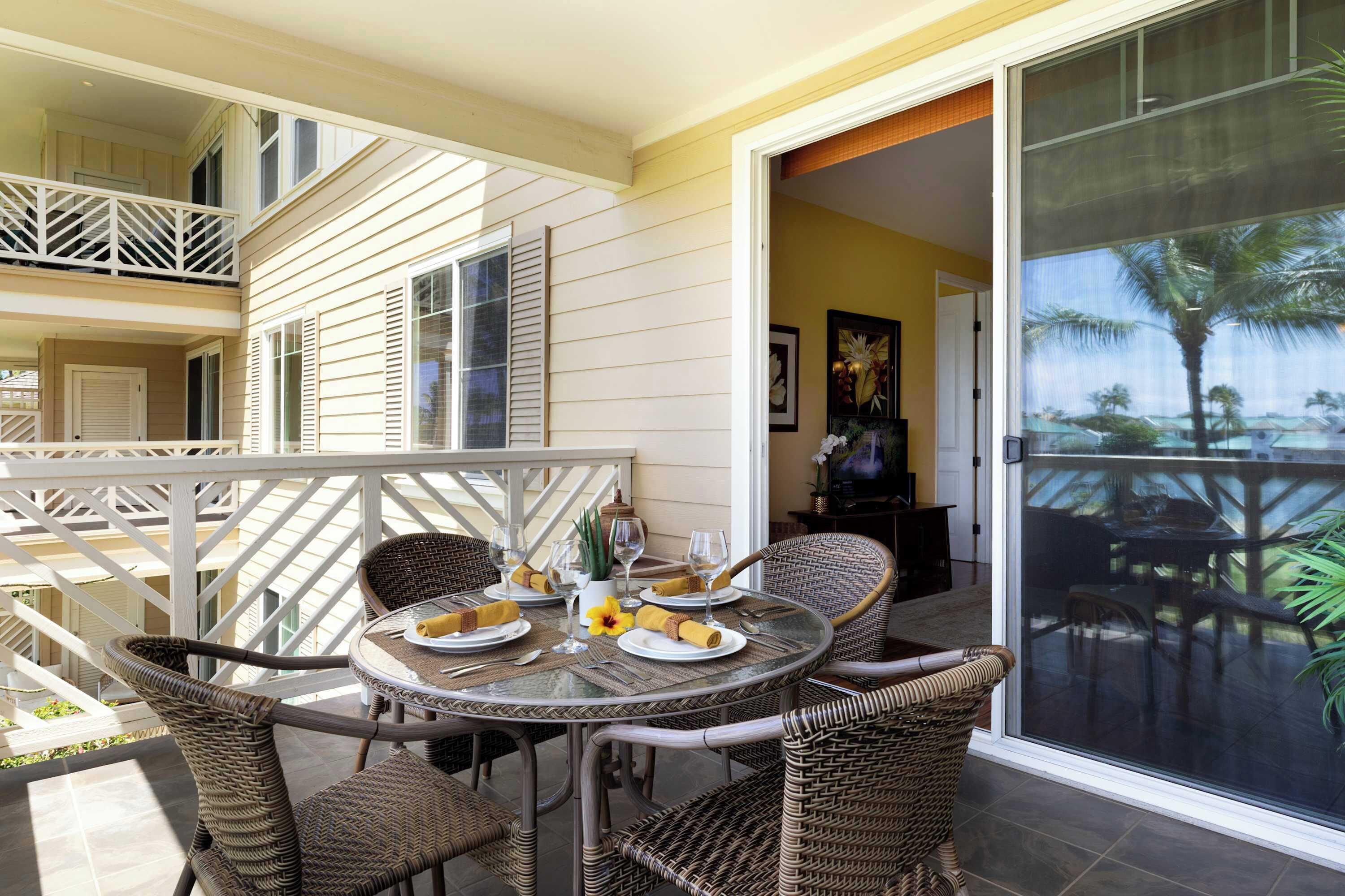A dining area with wicker chairs and a glass table set for four, featuring plates, cutlery, and a vase with flowers.