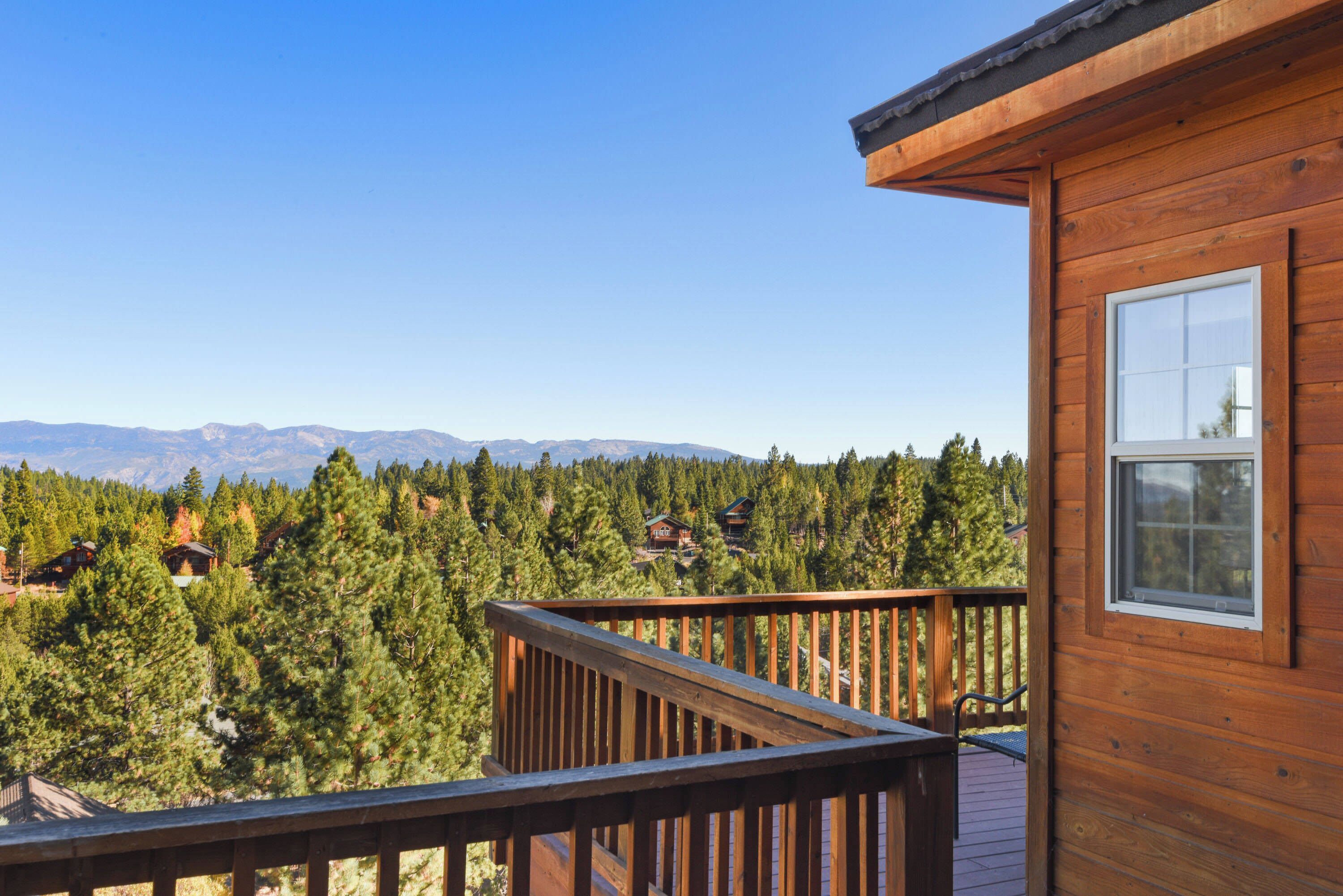 A wooden cabin with a deck overlooking a forest and mountains.