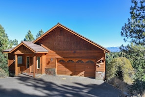 Een houten lodge met een garage, veranda en een berg op de achtergrond.