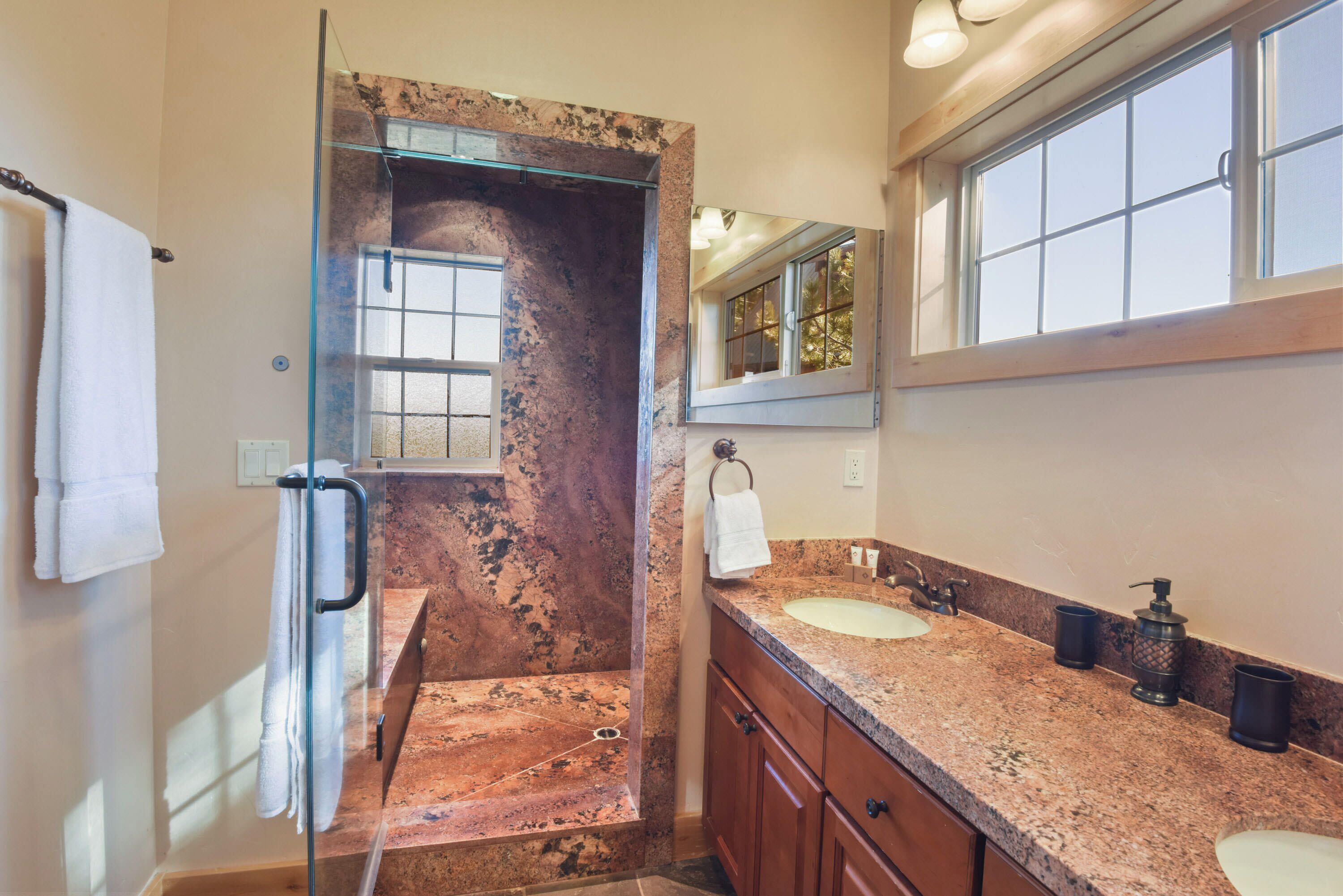 A bathroom with a glass shower enclosure, a marble countertop, a sink, and a mirror.