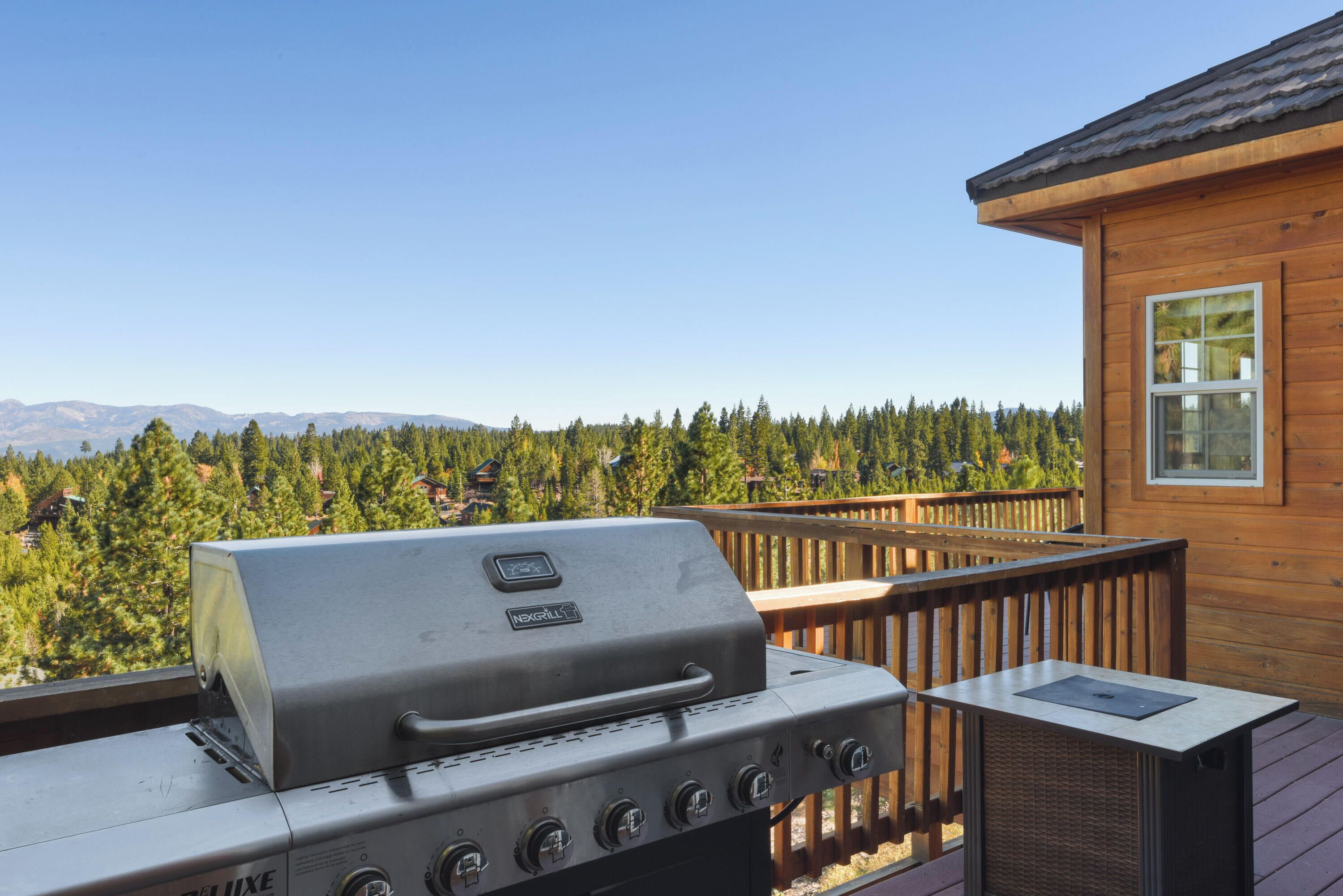 A grill on an outdoor deck with a view of a forest and mountains.