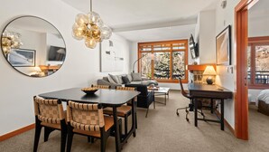 Una sala de estar moderna con comedor, un conjunto de sofá, televisor y un ventanal con vistas a árboles.