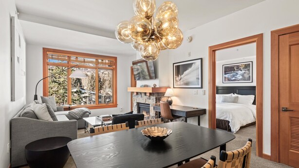 Una sala moderna con una mesa de comedor, sofá y sillas. Hay una chimenea, un televisor y cuadros en la pared.