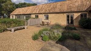 A two-story stone house with a tiled roof, a front door, and a small patio area with a table and chairs. - 1 bedroom accommodation in Clopton, near Kettering (Clopton, near Kettering)