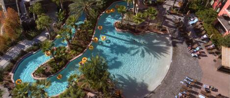 Relax by the resort pool surrounded by lush greenery and palm trees, with lounge chairs and umbrellas nearby.