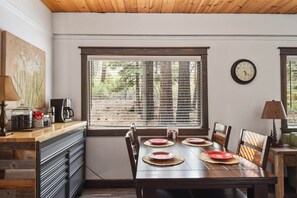 A dining area with a wooden table set for four, a window with blinds, a clock on the wall, and a coffee maker on the counter. - Incline Cottage Year-round Outdoor Fun! (Incline Village)