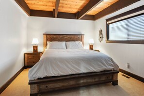 A bedroom with a wooden bed, two bedside tables with lamps, a window with blinds, and a wooden ceiling. - Incline Cottage Year-round Outdoor Fun! (Incline Village)