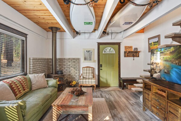 A cozy living room with a green sofa, a wooden coffee table, a fireplace, a television, and a green door. - Incline Cottage Year-round Outdoor Fun! (Incline Village)