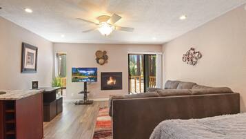 A spacious living area with a fireplace, a ceiling fan, and a large window.