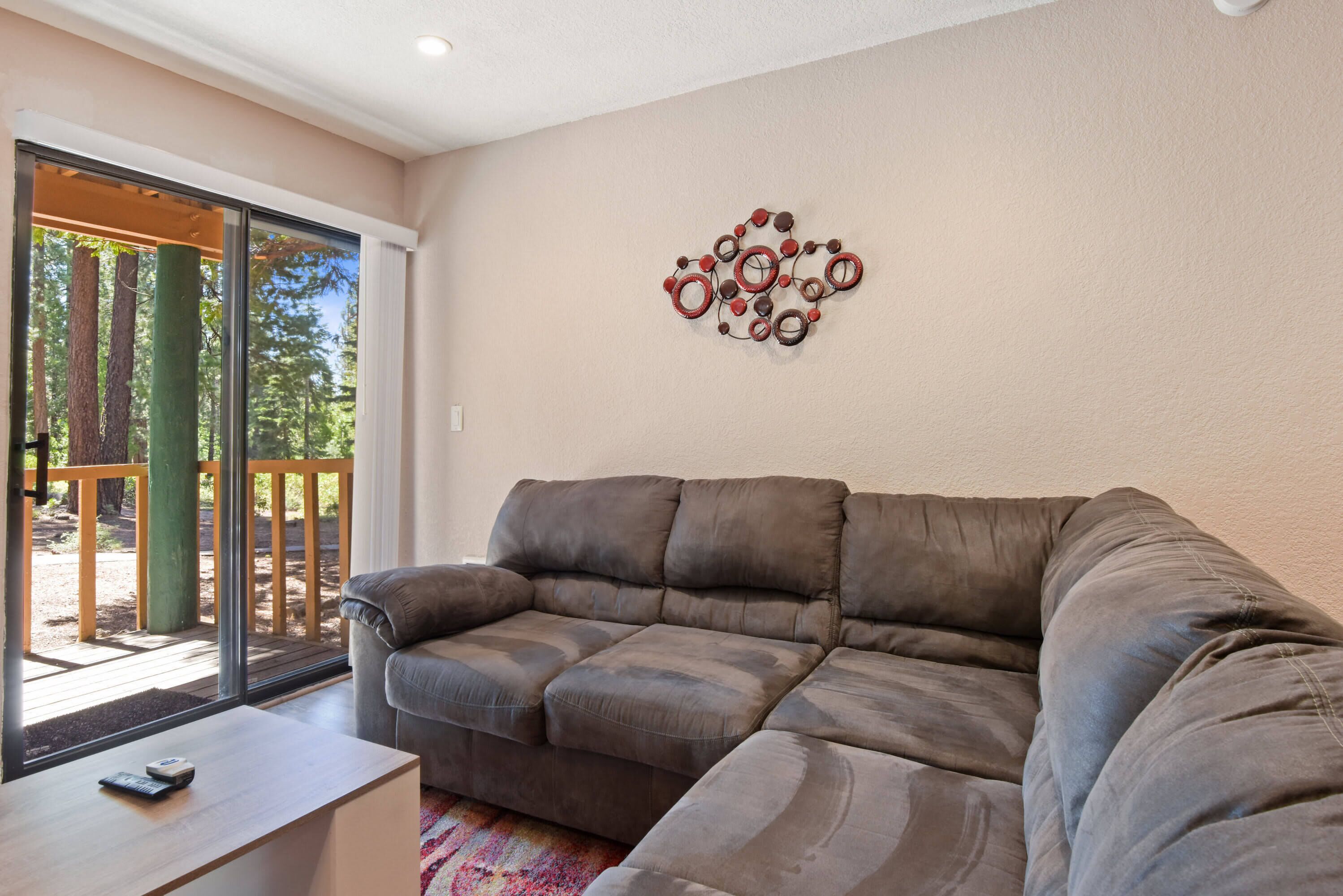 A modern living room with a grey sectional sofa, a wooden coffee table, and a wall-mounted abstract art piece.