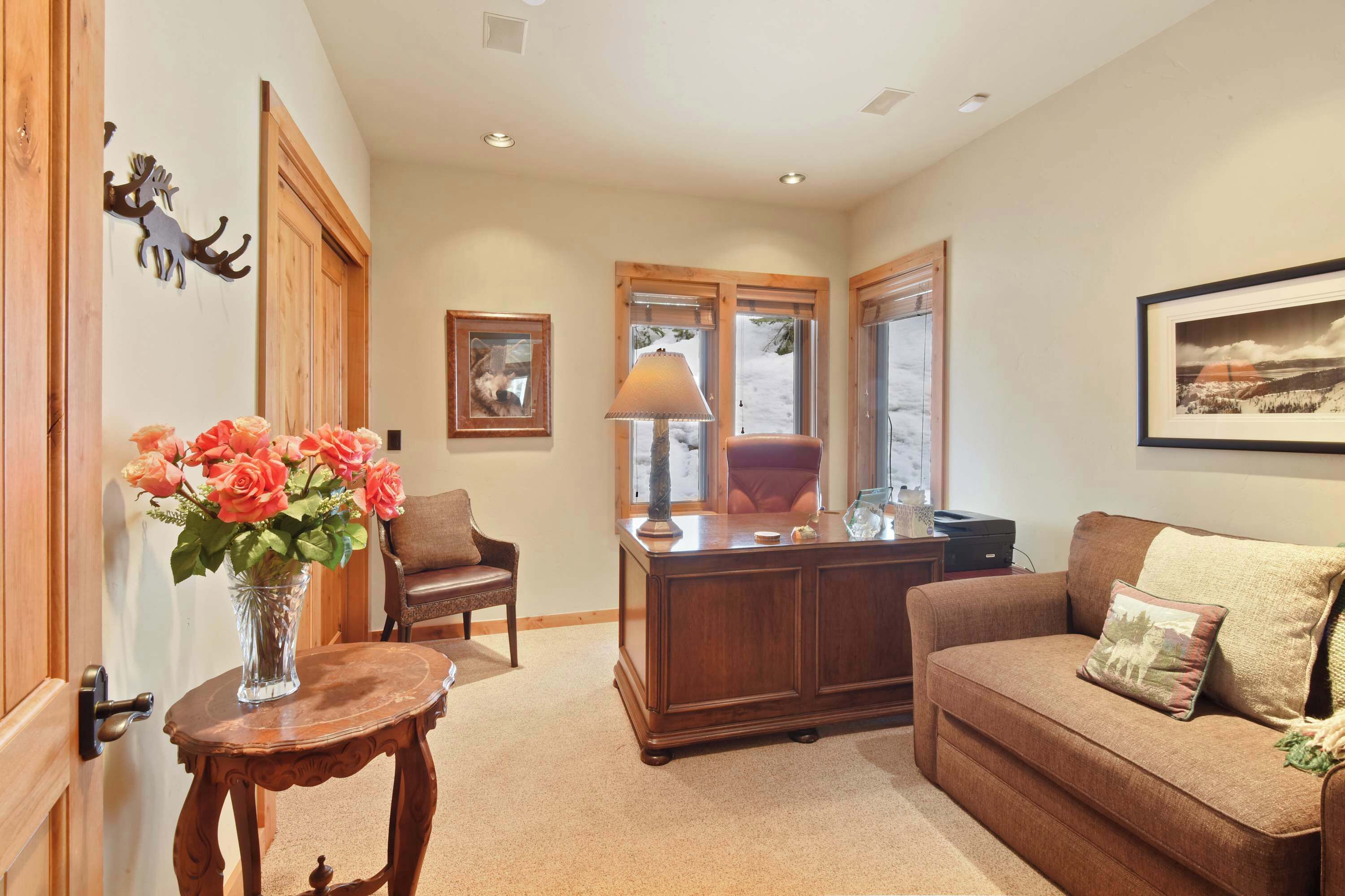 A cozy living room with a wooden desk, a brown sofa, and a vase of flowers.