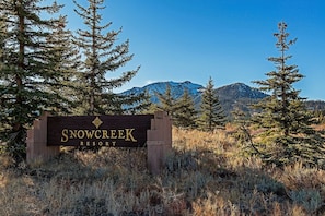 A sign for Snow Creek Resort surrounded by tall evergreen trees and mountains in the background. - Snowcreek #630 - Near Lakes & Golf! (Mammoth Lakes)