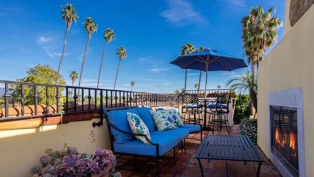 A terrace with a blue sofa, a table, chairs, a fire pit, and tall palm trees. - Luxurious Mykonos - Pet Friendly (Santa Barbara)