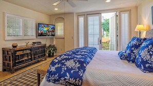 A bedroom with a bed, a television, a ceiling fan, and a view of the outdoors through a door. - Luxurious Mykonos - Pet Friendly (Santa Barbara)