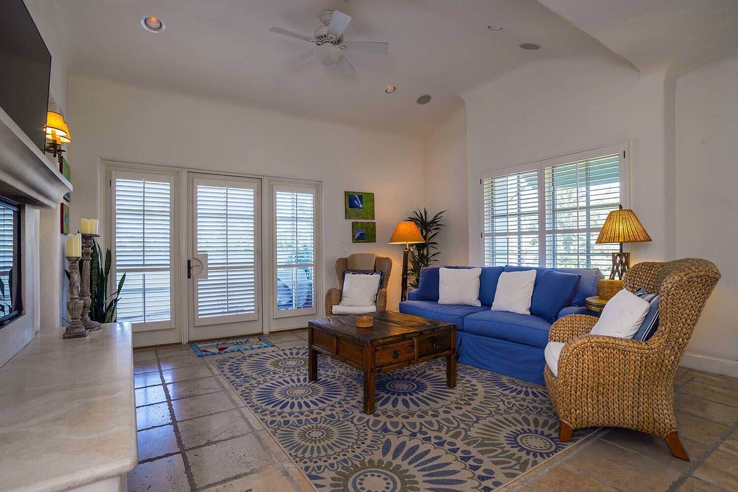 A living room with a blue sofa, a wicker chair, a coffee table, and a patterned rug.