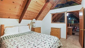 Una camera da letto con soffitto in legno, un letto con copriletto decorato, un comodino, una scrivania e una finestra.