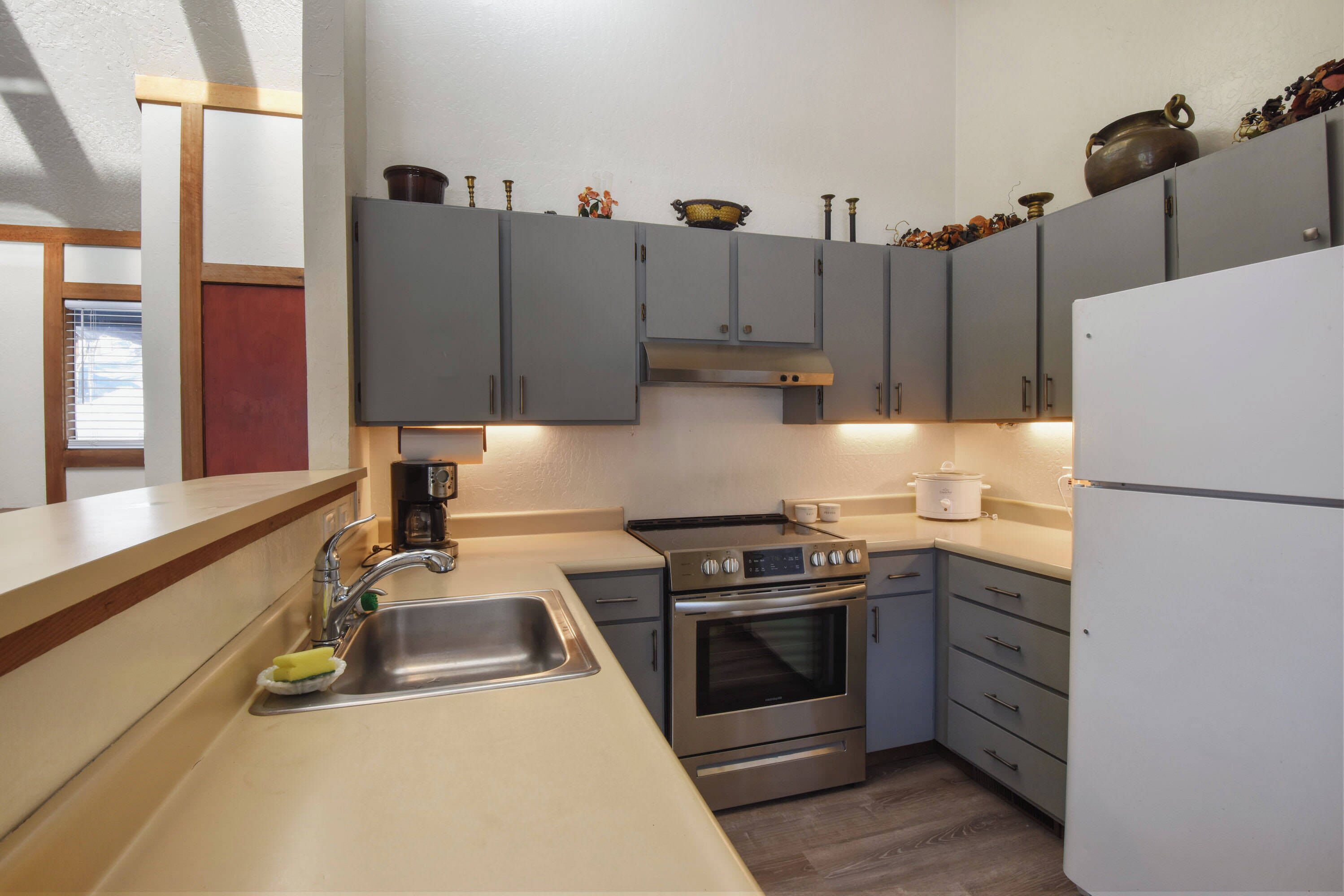 A modern kitchen with grey cabinets, stainless steel appliances, and a wooden countertop.