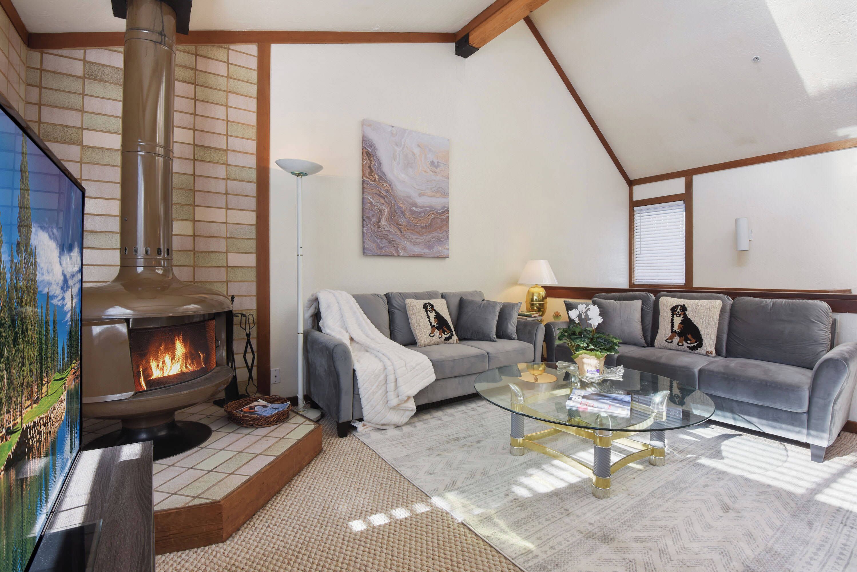 A living room with a fireplace, a sofa set, a glass coffee table, and a painting on the wall.