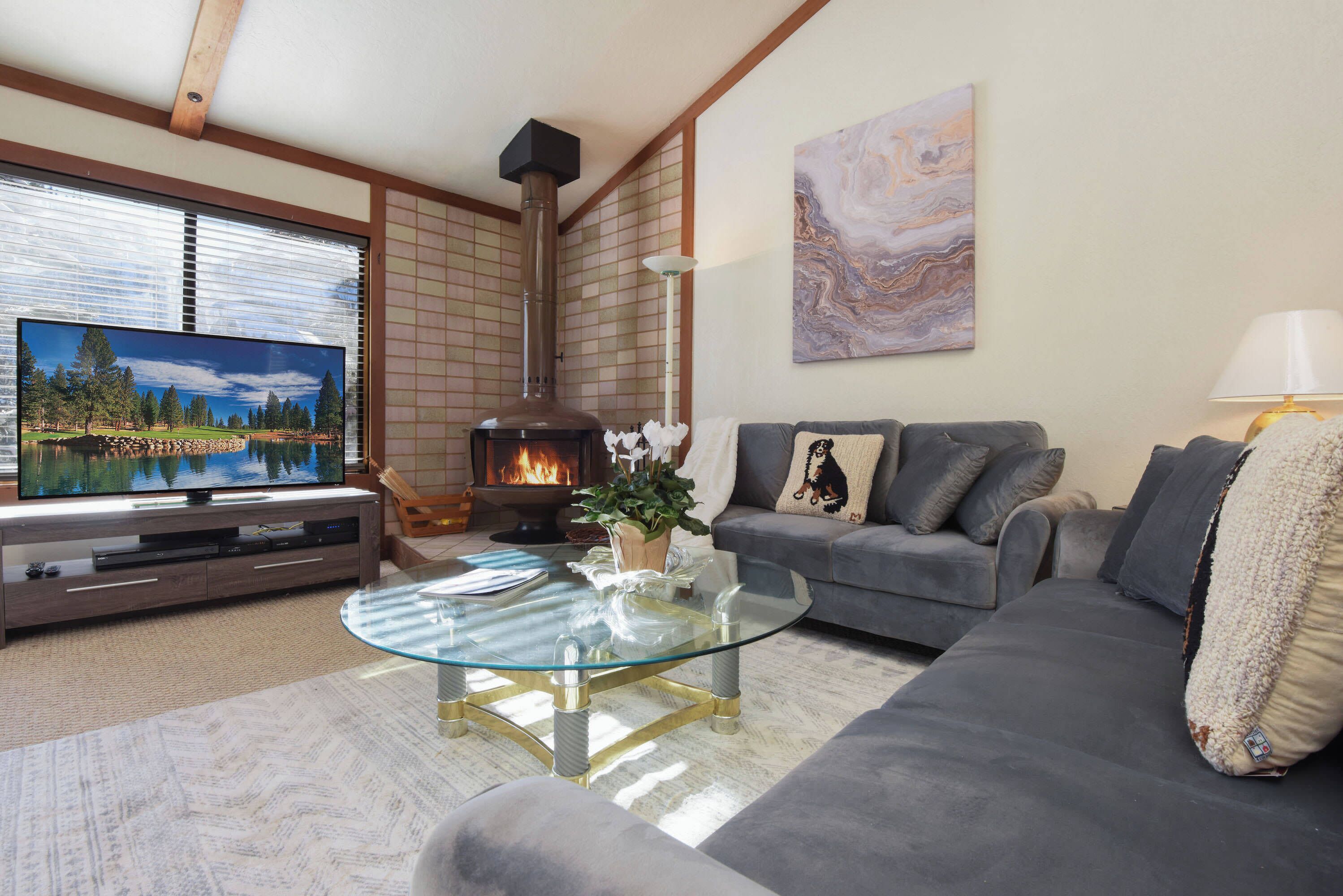 Ein Wohnzimmer mit Kamin, einer Couch, einem Glastisch und einem Fernseher, der eine schöne Landschaft zeigt.