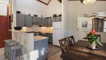 A kitchen with grey cabinets, a white refrigerator, and a wooden dining table with a potted plant.